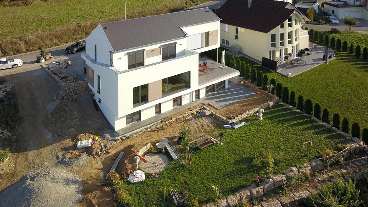 Außenaufnahme eines modernen Neubau-Einfamilienhaus mit weißer Fassade und Holzelementen zwischen den Fenstern und Terrassen.