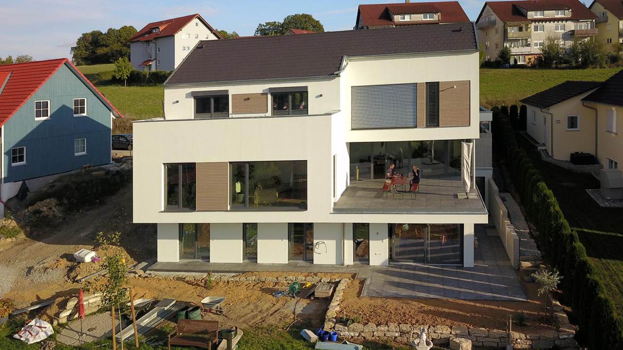Außenaufnahme eines modernen Neubau-Einfamilienhaus mit weißer Fassade und Holzelementen zwischen den Fenstern und Terrassen.